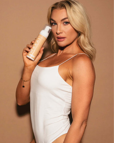 Woman holding a bottle of self tanner against a beige background