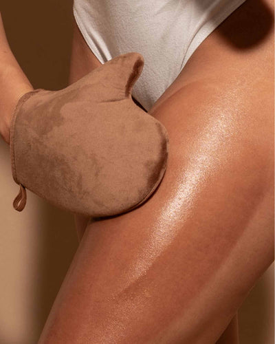 Person using a brown exfoliating glove on their arm with a neutral background