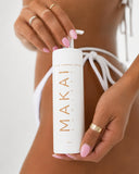 Person holding a white bottle of MAKAI tanning lotion with a blurred background