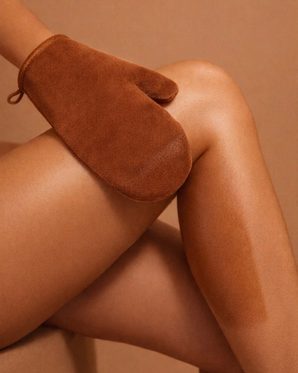 Brown self tanning mitt on a person's hand with a neutral background