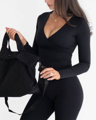 Woman holding a black bag wearing a black outfit on a white background