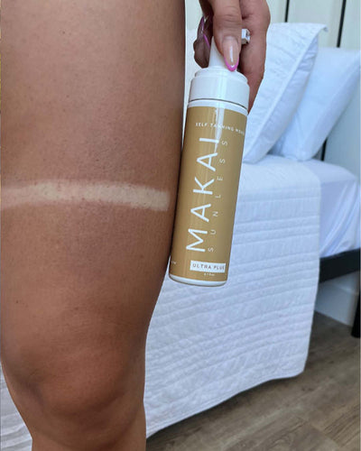 Person applying Makai Sunless tanning mist to their skin with a white background.