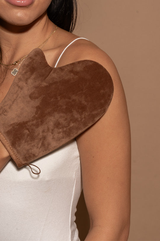 Brown self tanning mitt applying self tanner to shoulder shoulder against a beige background